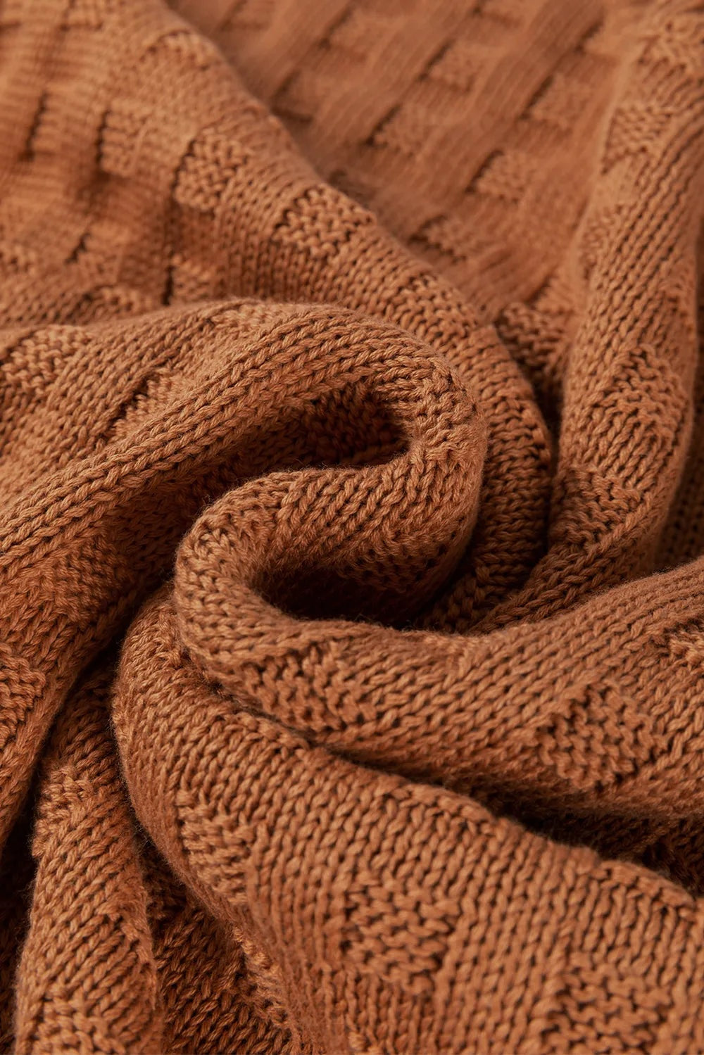 Close-up of a brown knitted sweater fabric, highlighting its soft textured construction, chunky yarn, and gently folded drape.