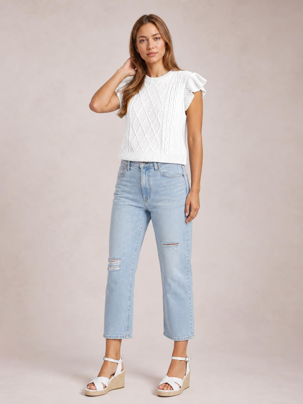A model poses in a white round neck cap sleeve sweater with ruffled shoulders, cable-knit texture, ribbed trim, and a straight cropped silhouette.