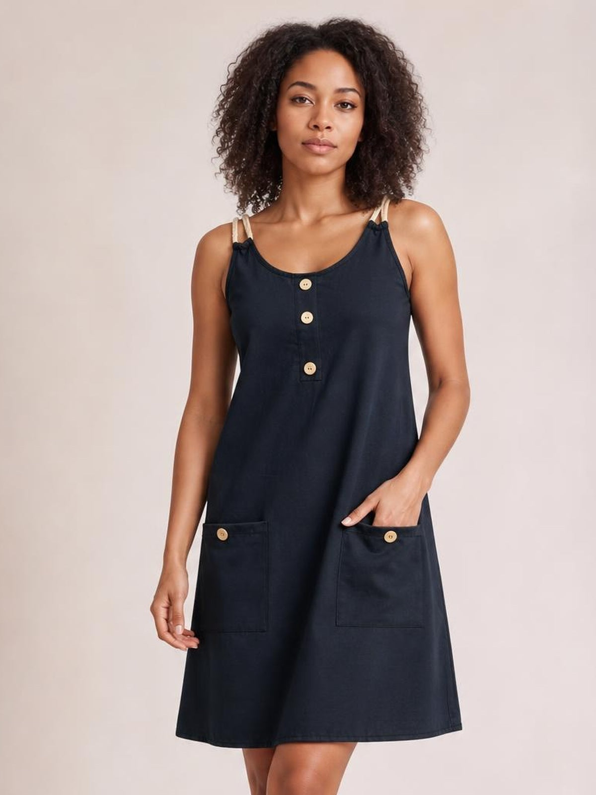 A model stands in a navy round-neck mini dress with double spaghetti straps, decorative front buttons, two patch pockets, and a relaxed A-line silhouette.