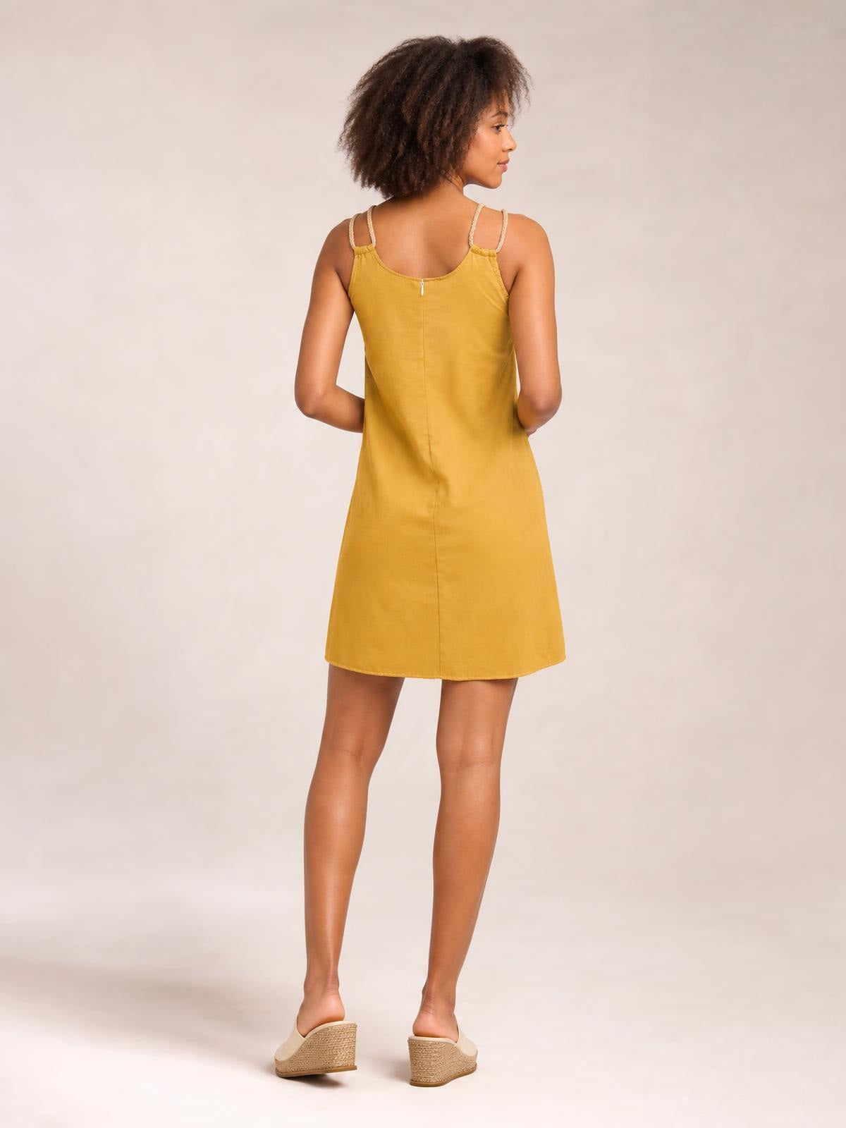 Model shown from the back in a mustard yellow mini dress with a round neck, double spaghetti straps, and a straight A-line silhouette.