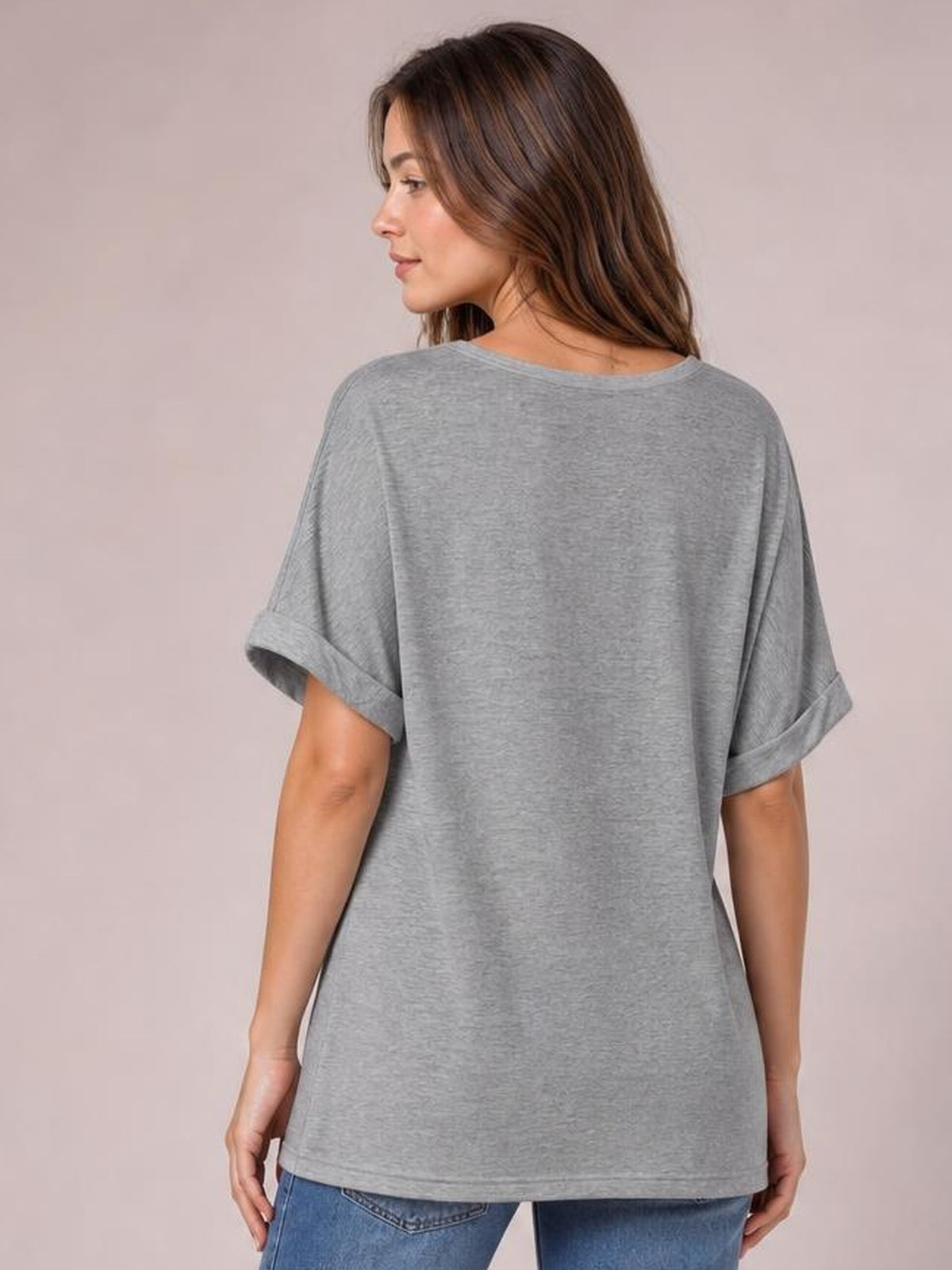 Model turned slightly to show the back of a gray round neck half sleeve T-shirt with rolled cuffs and a relaxed, straight silhouette.