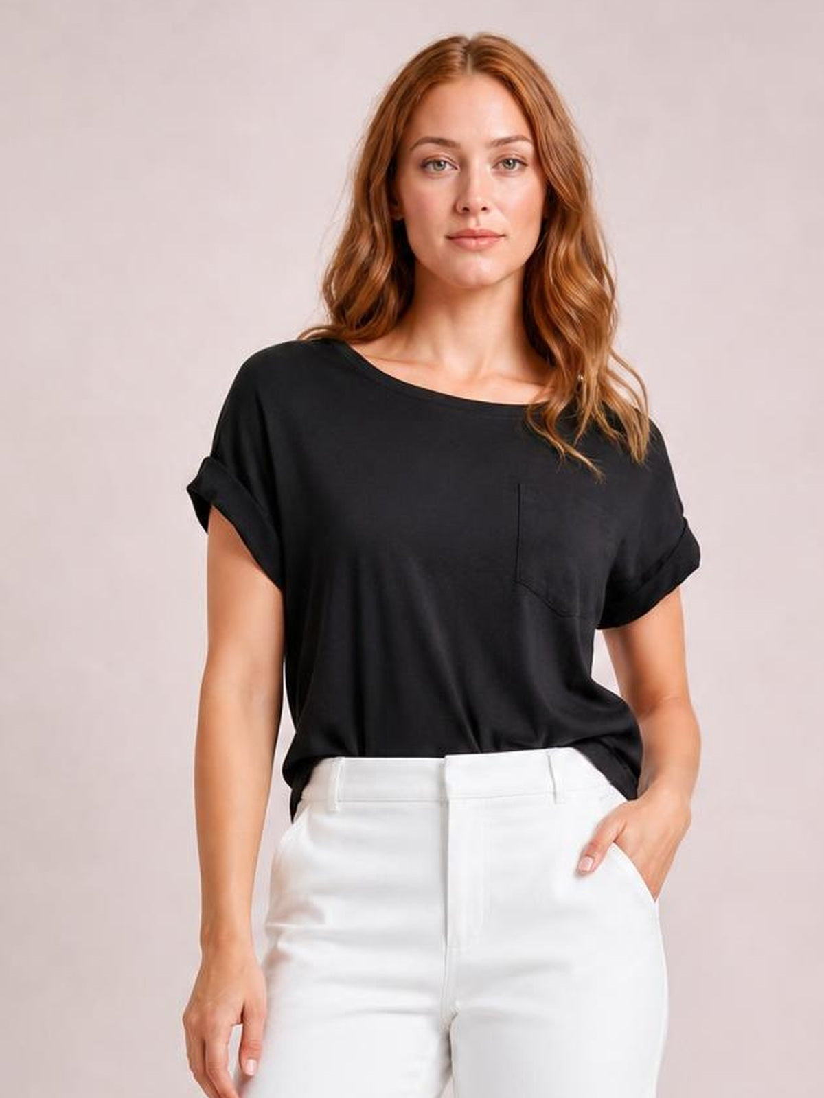 Model wearing a black round neck half sleeve T-shirt with rolled cuffs, relaxed silhouette, and visible chest pocket, posing with one hand in her pocket.