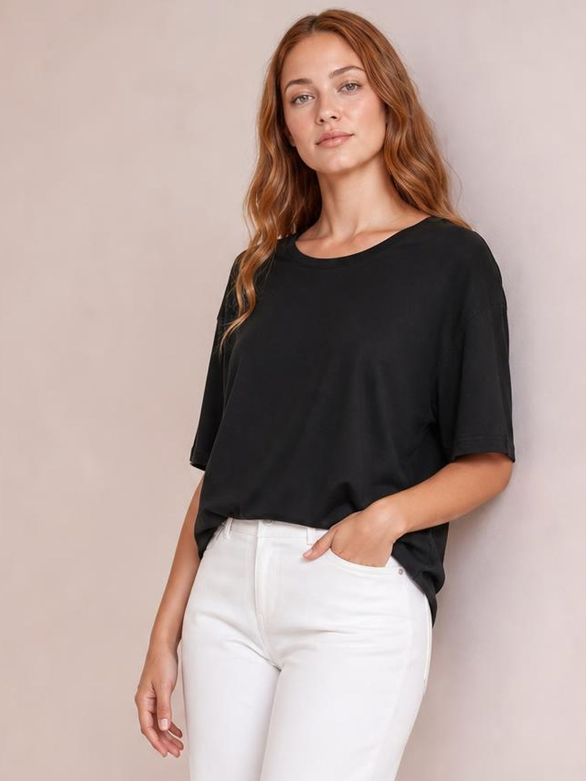 A model wears a black round neck half sleeve T-shirt with a relaxed silhouette, slightly loose fit, and straight hem while posing with one hand in her pocket.