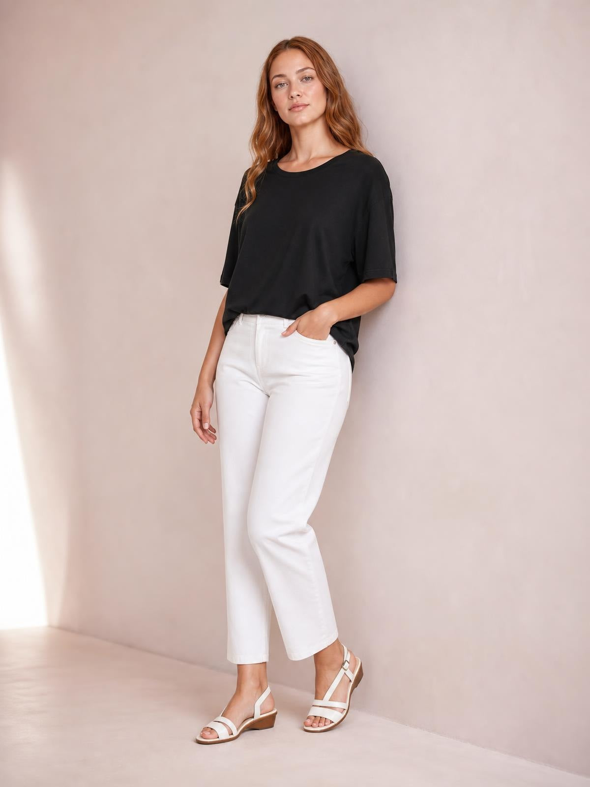 Model wearing a black round neck half sleeve T-shirt with a relaxed silhouette and visible pocket, posed with one hand in her white pants pocket.