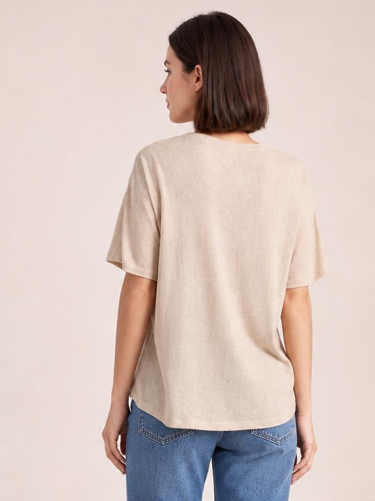 A model faces away wearing a beige round neck half sleeve T-shirt with a relaxed, slightly loose silhouette and curved hem.