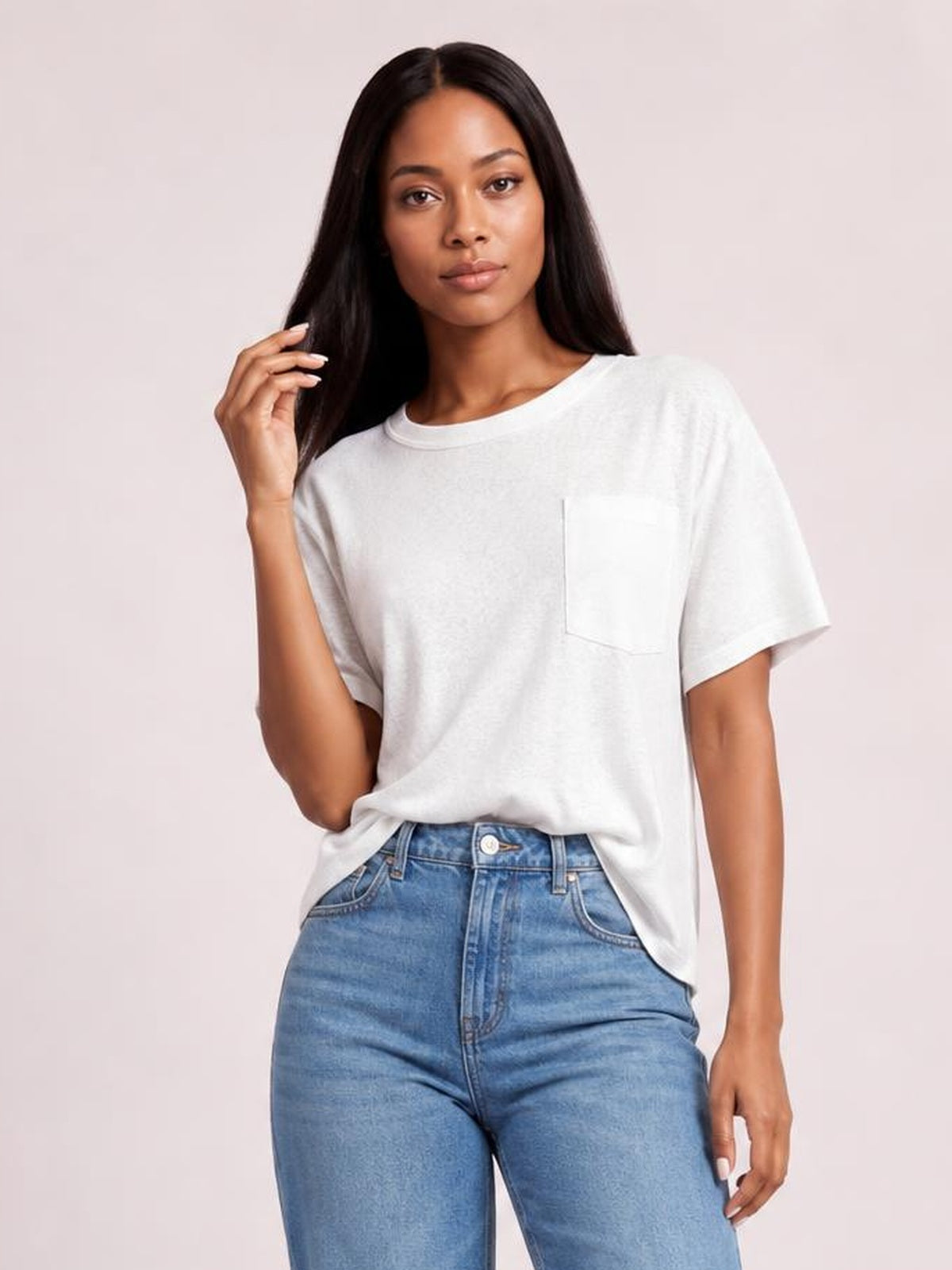 A model poses in a white round neck half sleeve T-shirt with a relaxed silhouette, short sleeves, and a single chest pocket, partly tucked into jeans.