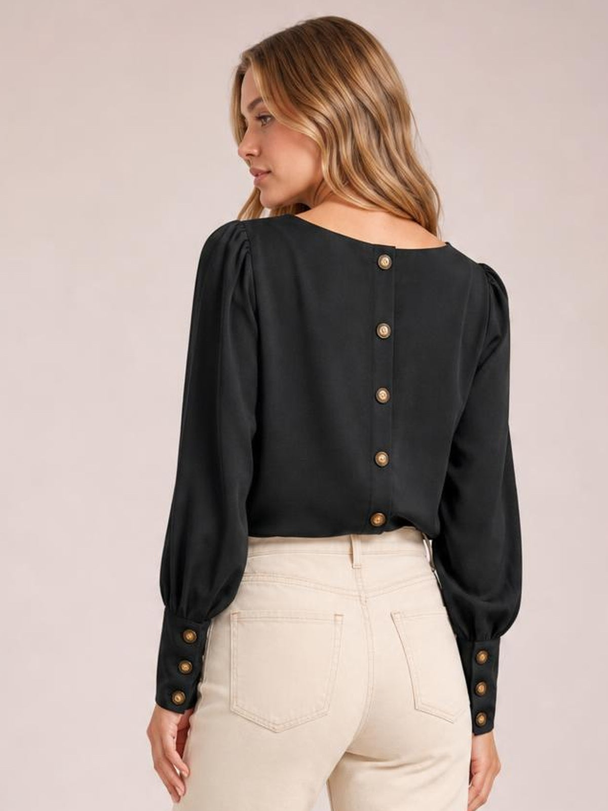 A model looks over her shoulder wearing a black round neck blouse with lantern sleeves, buttoned back placket, gathered shoulders, and buttoned cuffs.