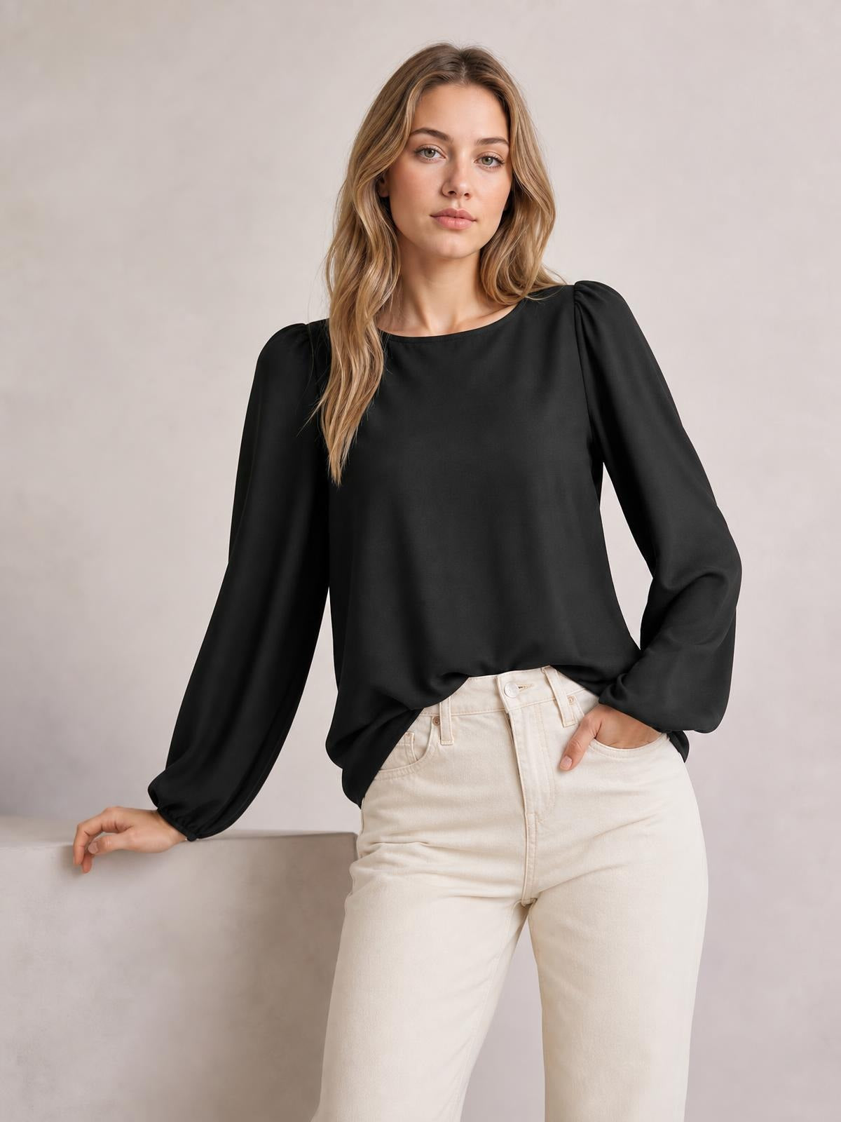 A model poses in a black round-neck blouse with gathered lantern sleeves, a relaxed straight silhouette, and elasticized cuffs, paired with cream pants.