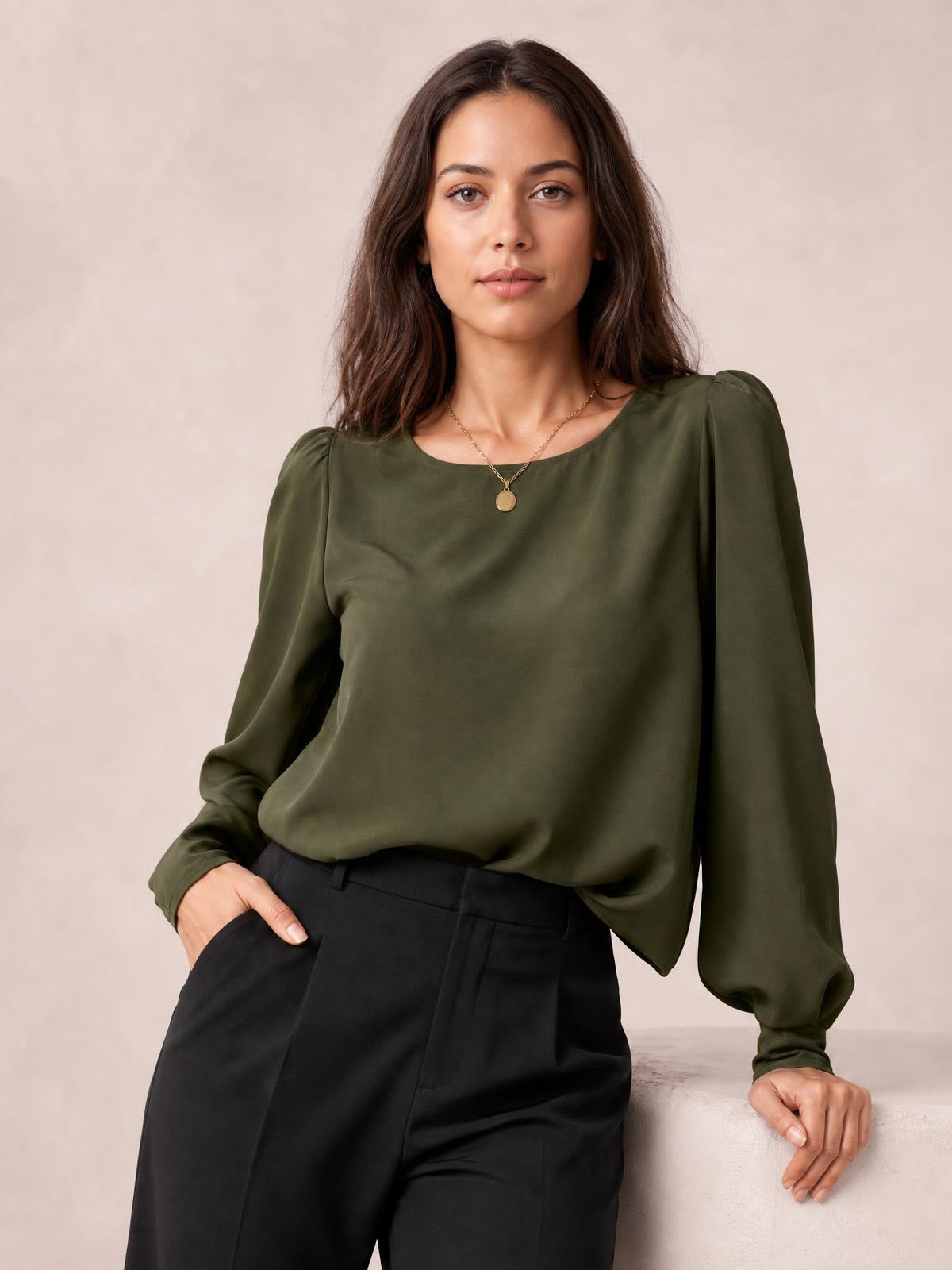 Model wearing an olive green round neck blouse with long lantern sleeves, gathered cuffs, and a relaxed draped silhouette, posing with one hand in her pocket.