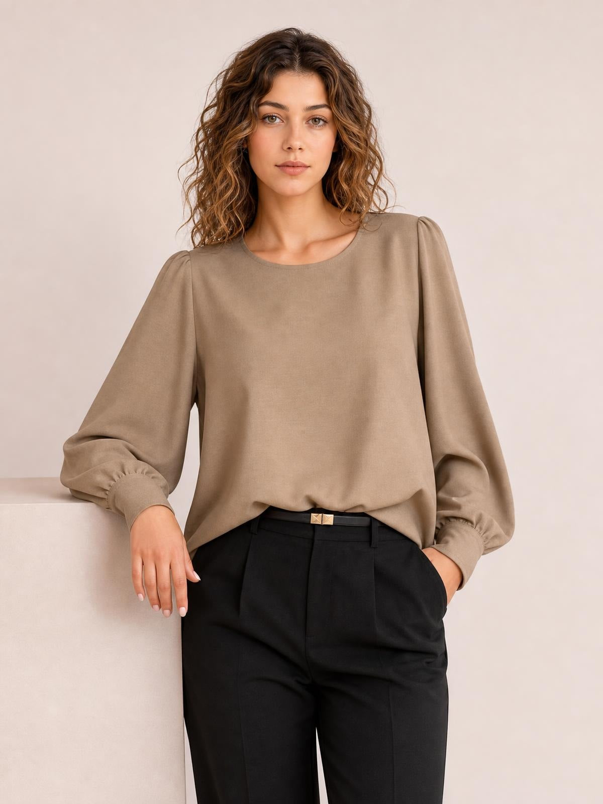 Model wearing a taupe round neck blouse with voluminous lantern sleeves, gathered cuffs, and a relaxed straight silhouette tucked into black trousers.