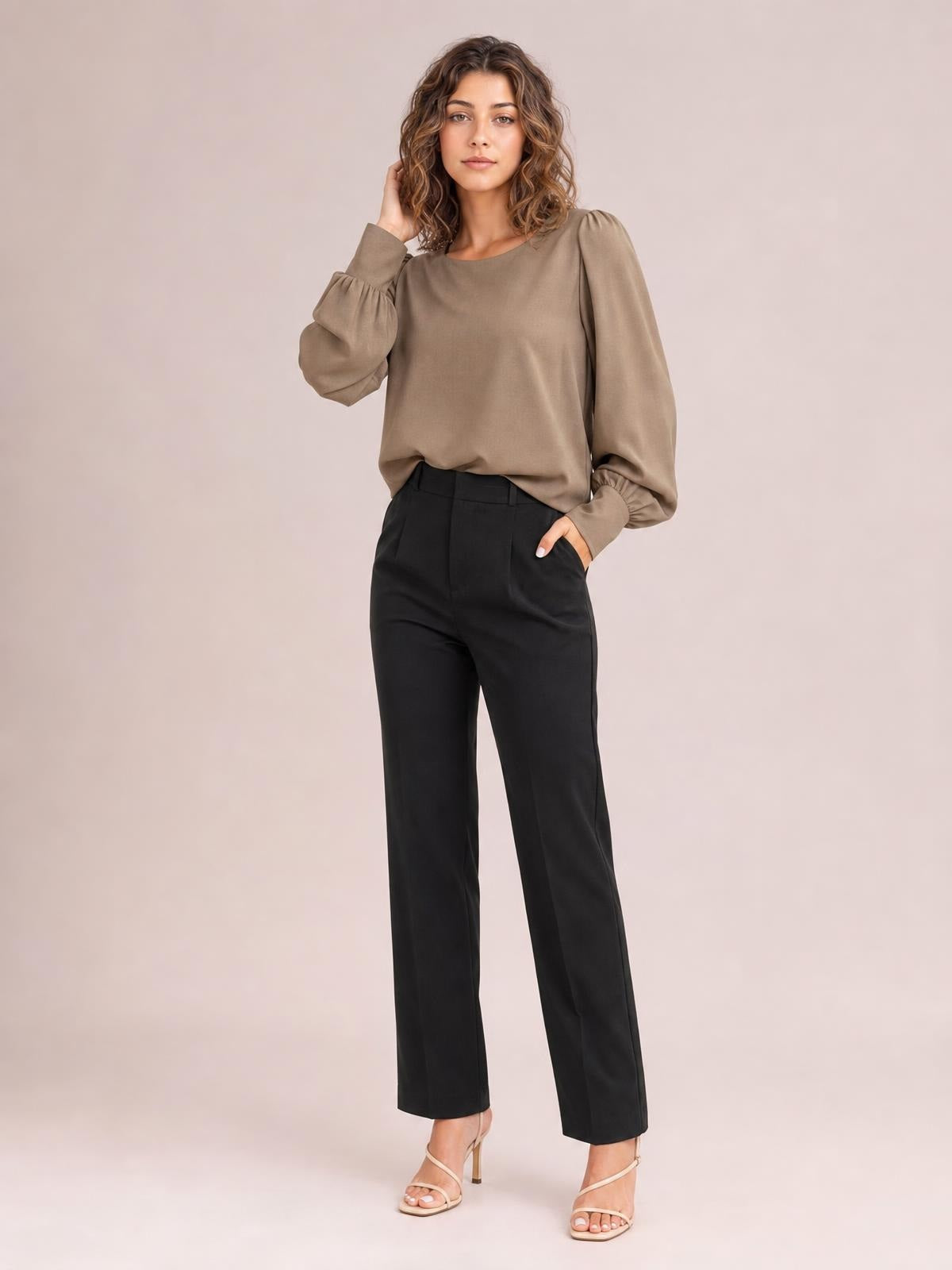 Model wears a taupe round neck blouse with voluminous lantern sleeves, gathered cuffs, and a relaxed silhouette while standing with one hand in her pocket.