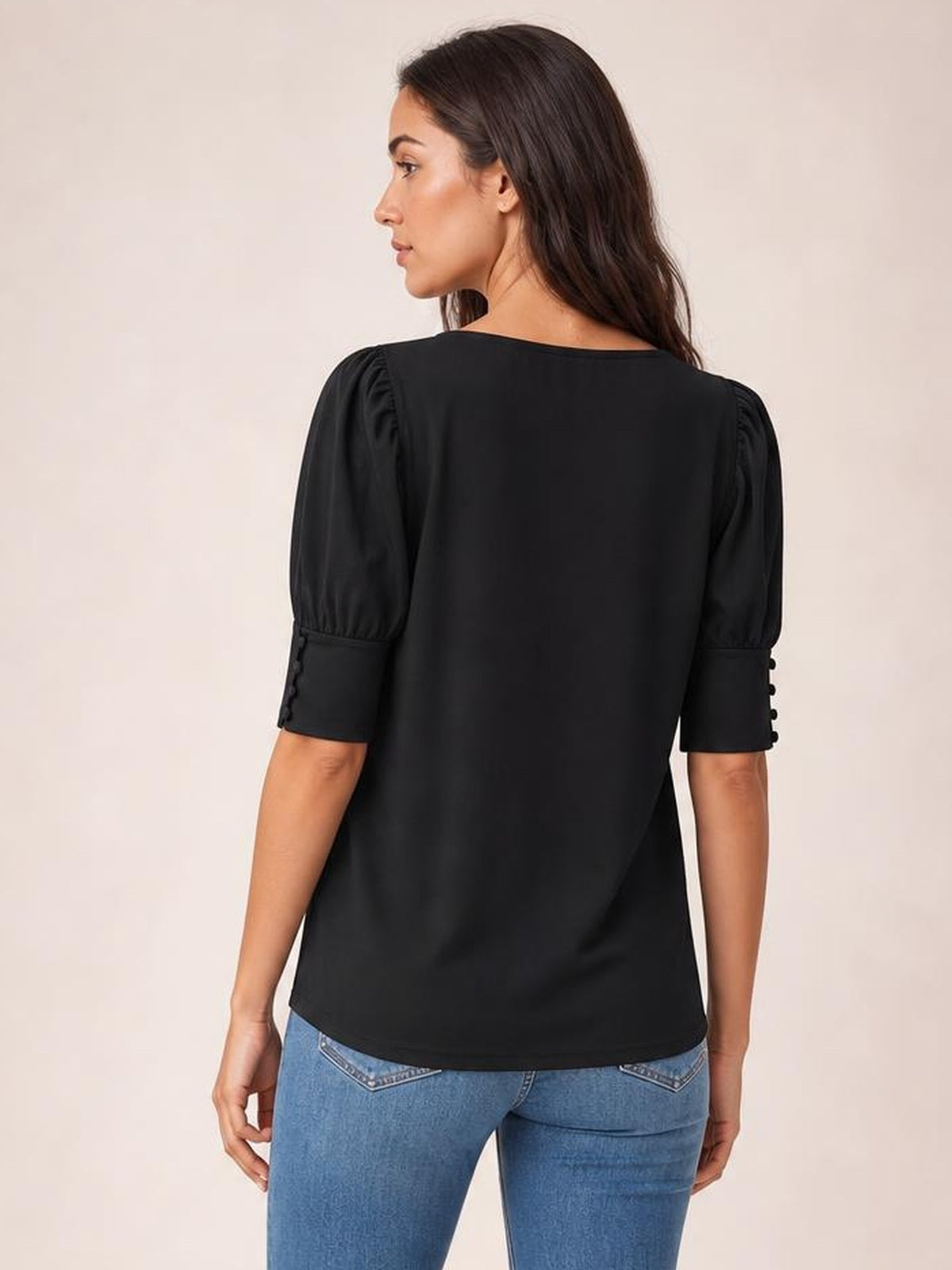 Model shown from the back wearing a black round neck blouse with lantern sleeves, gathered shoulders, buttoned cuffs, and a relaxed straight silhouette.