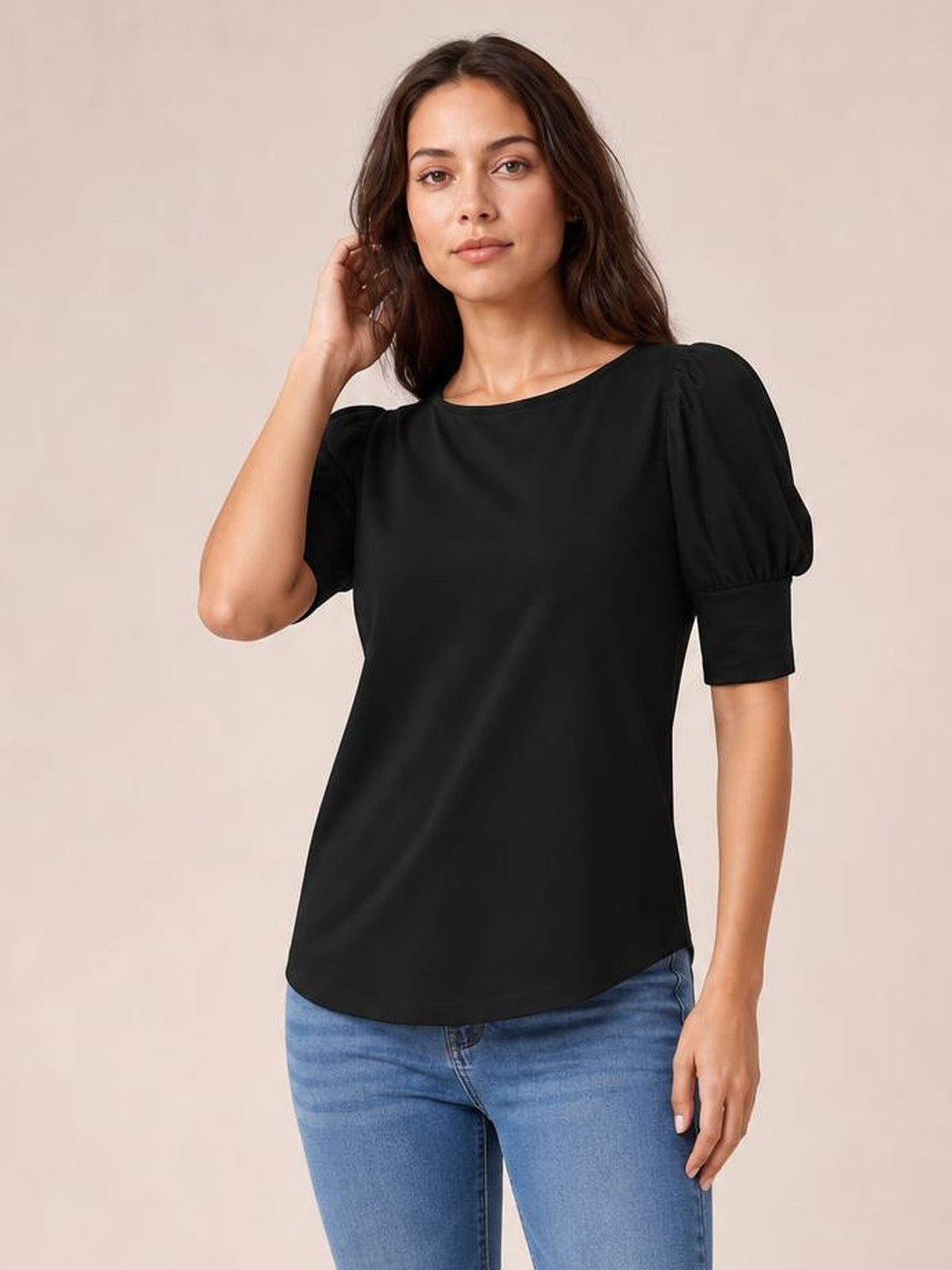 A model poses in a black round neck blouse with puffed lantern sleeves, cuffed short sleeves, and a relaxed straight silhouette over blue jeans.