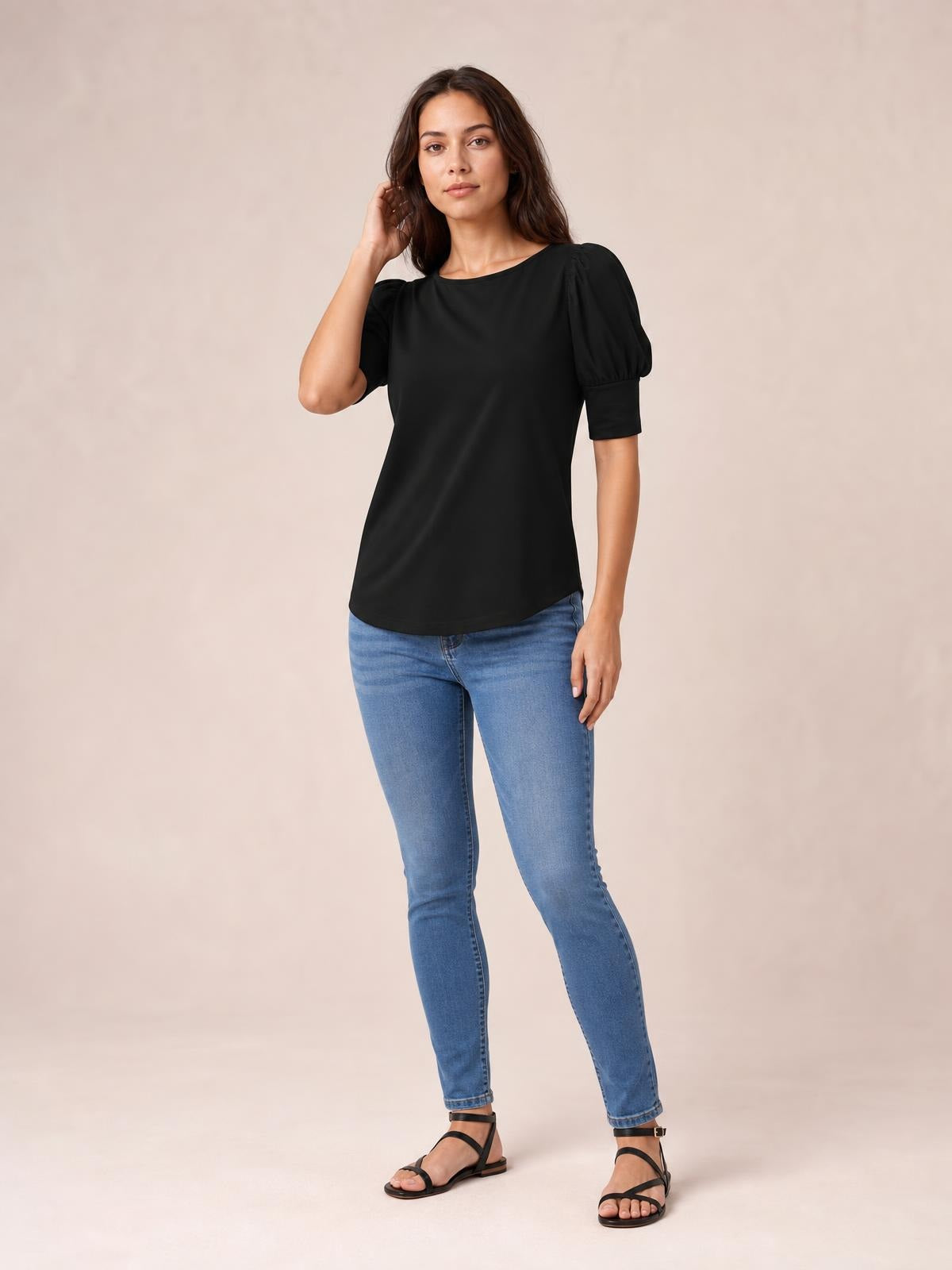 A model poses in a black round neck blouse with voluminous lantern sleeves, fitted cuffs, a relaxed straight silhouette, and a gently curved hem.