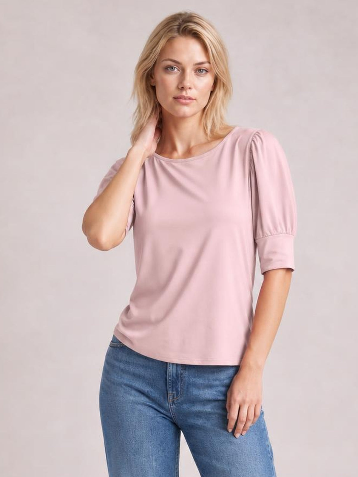 A model poses in a soft pink round neck lantern sleeve blouse with gathered shoulders, three-quarter sleeves, and a relaxed straight silhouette.