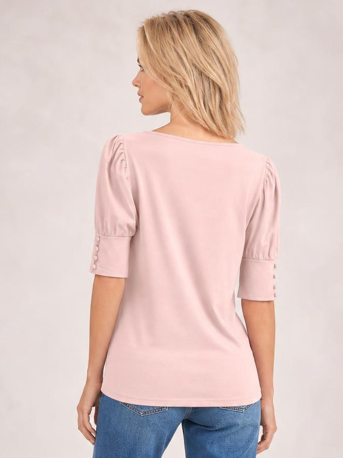 A model viewed from behind wears a pink round neck blouse with a smooth silhouette, gathered lantern sleeves, and buttoned elbow-length cuffs.