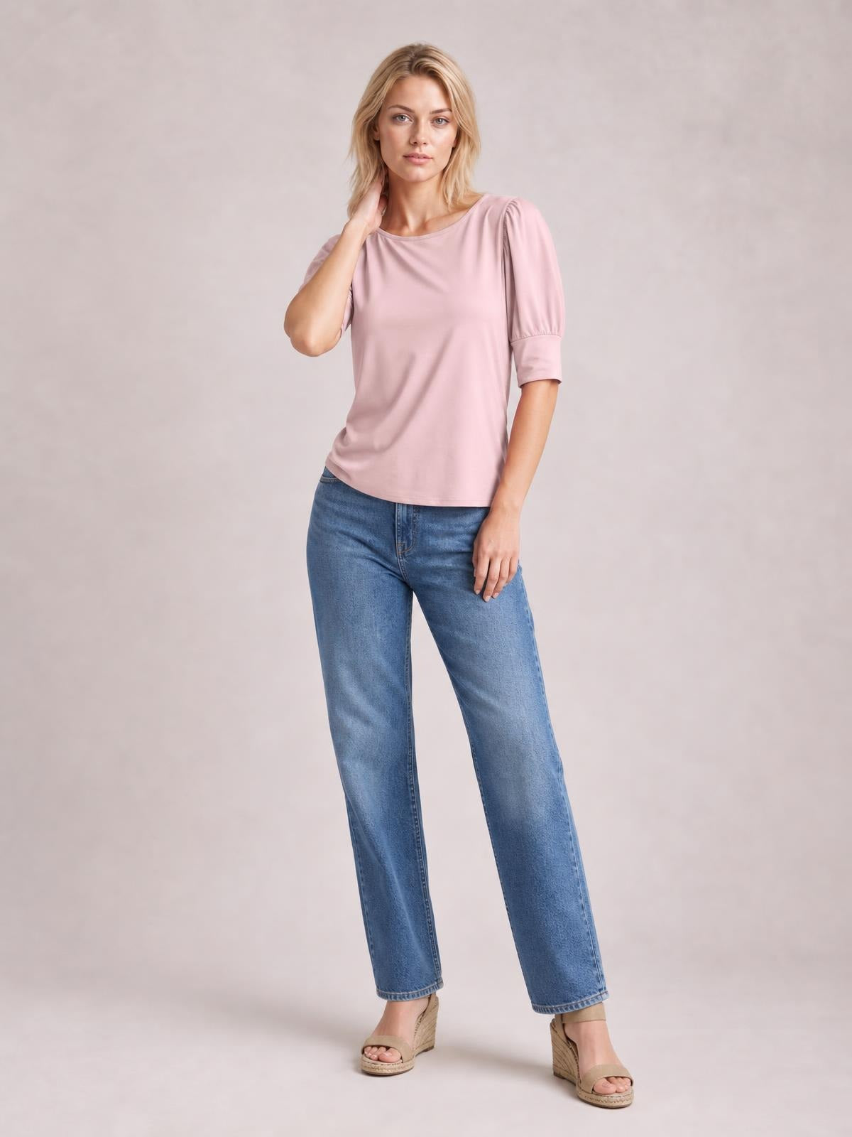 A model poses in a pink round neck blouse with gathered lantern sleeves, cuffed hems, and a relaxed straight silhouette, paired with blue jeans.
