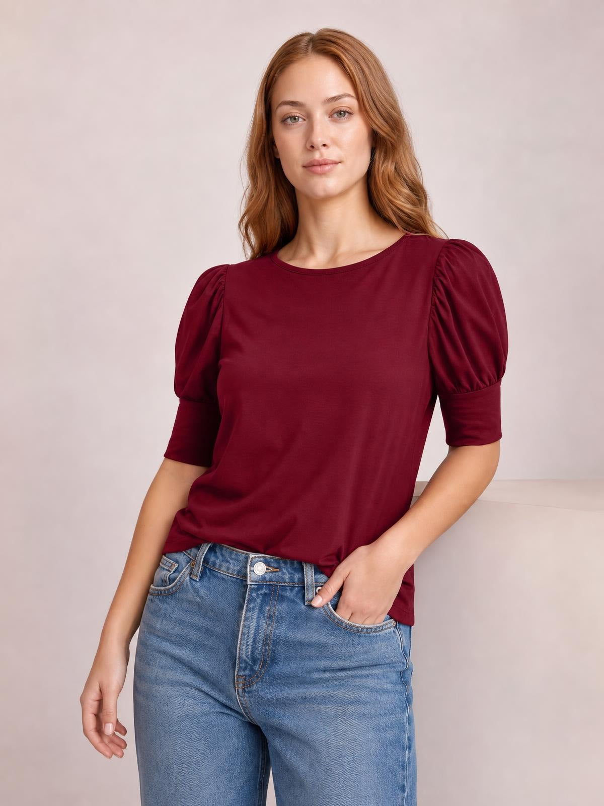 Model wearing a burgundy round neck blouse with gathered lantern sleeves, fitted cuffs, and a relaxed straight silhouette, paired with blue jeans.