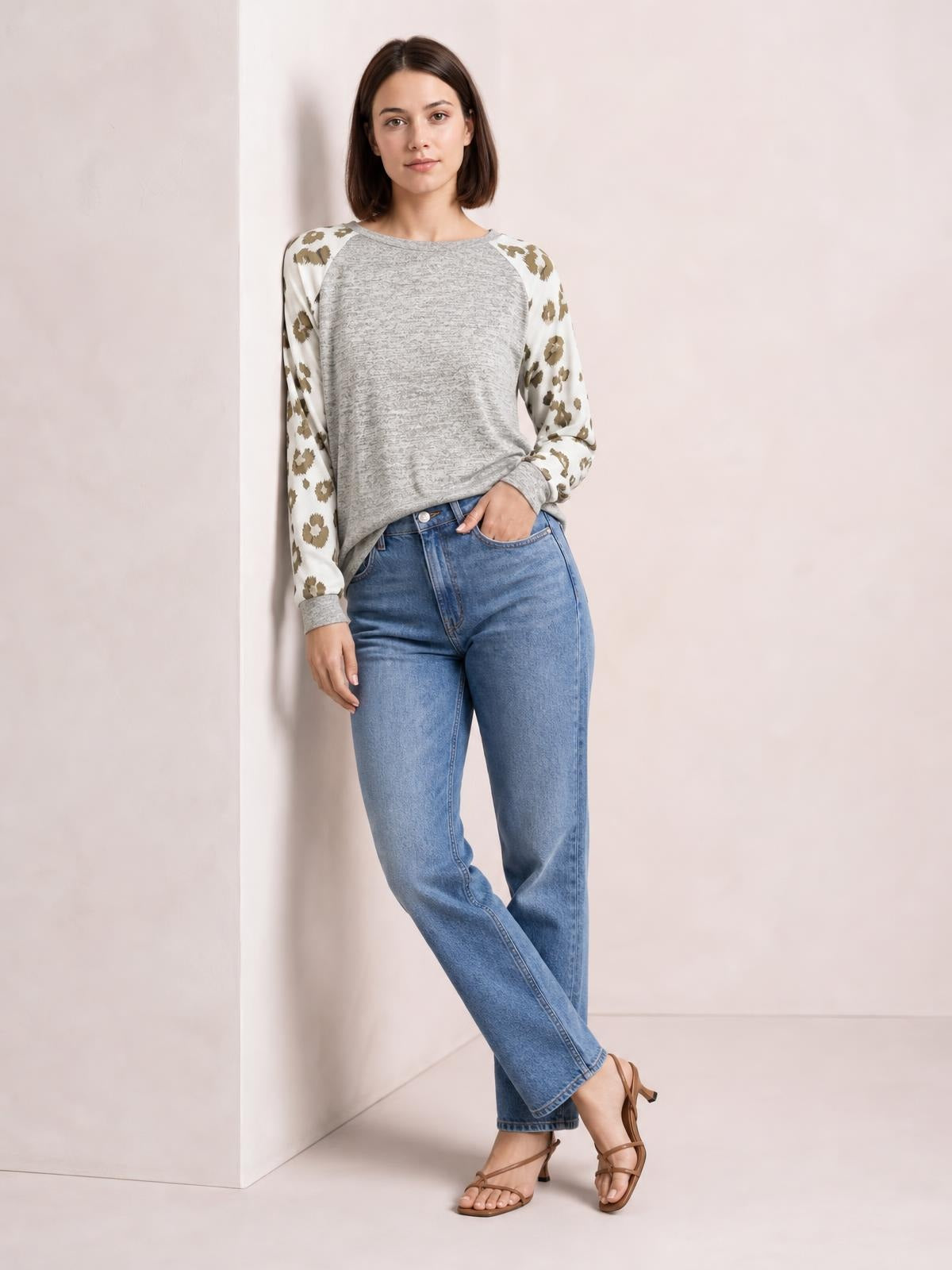 Model poses in a gray round neck top with white leopard print raglan sleeves, a relaxed silhouette, and ribbed cuffs.