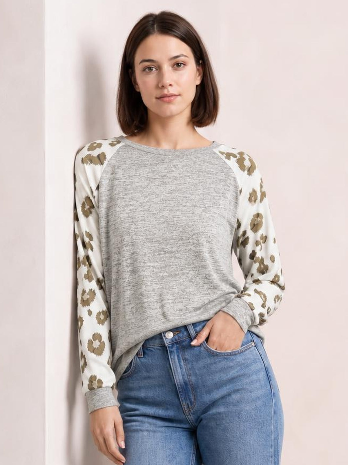 Model wears a gray round-neck leopard print raglan sleeve top with an easy straight silhouette, ribbed cuffs, and one hand resting in her jeans pocket.