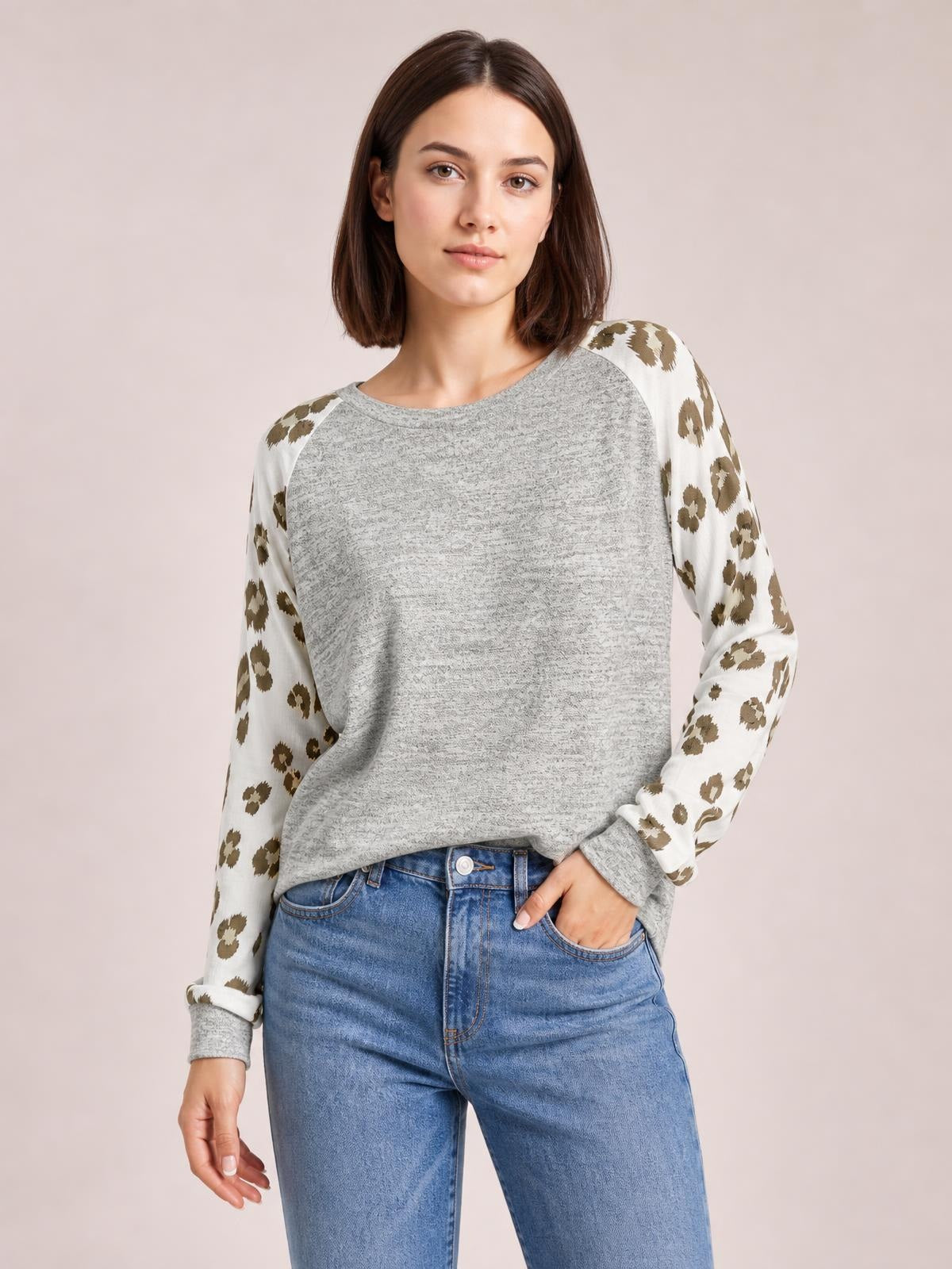 Model wearing a gray round neck leopard print raglan sleeve top with a relaxed silhouette, long sleeves, and one hand resting in her jeans pocket.