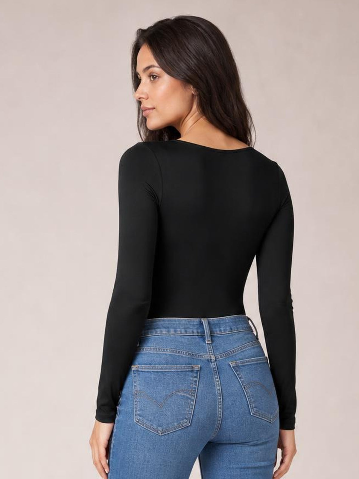 Model turned away wears a black round neck long sleeve bodysuit with a sleek fitted silhouette and smooth opaque construction.