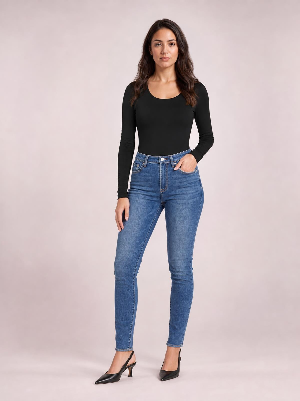 Model wears a black round neck long sleeve bodysuit with an opaque, fitted silhouette and moderate stretch, paired with jeans and one hand in a pocket.