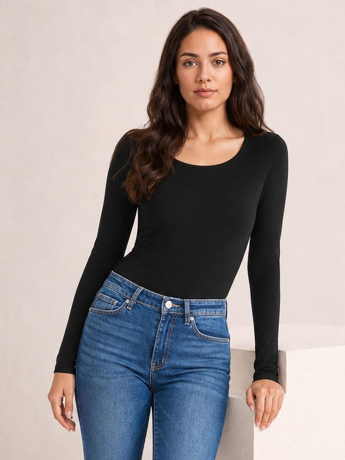 A model leans slightly in a black round neck long sleeve bodysuit with a smooth, fitted silhouette and moderate stretch.