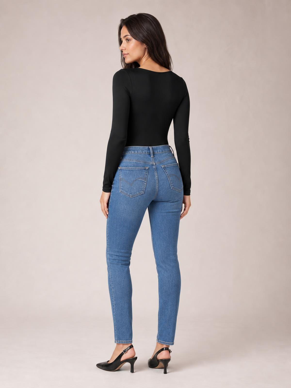 Model turns to show the black round neck long sleeve bodysuit’s smooth, fitted silhouette and full back coverage with moderate stretch.