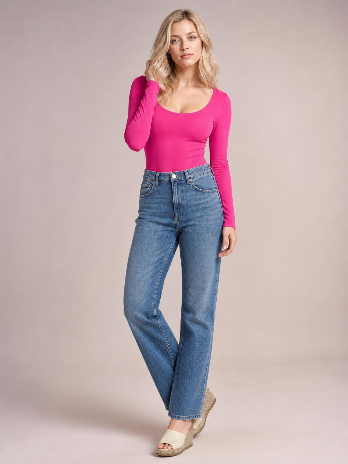 Model wears a bright pink round-neck long-sleeve bodysuit with a fitted silhouette and moderate stretch, posing with one hand near her hair.