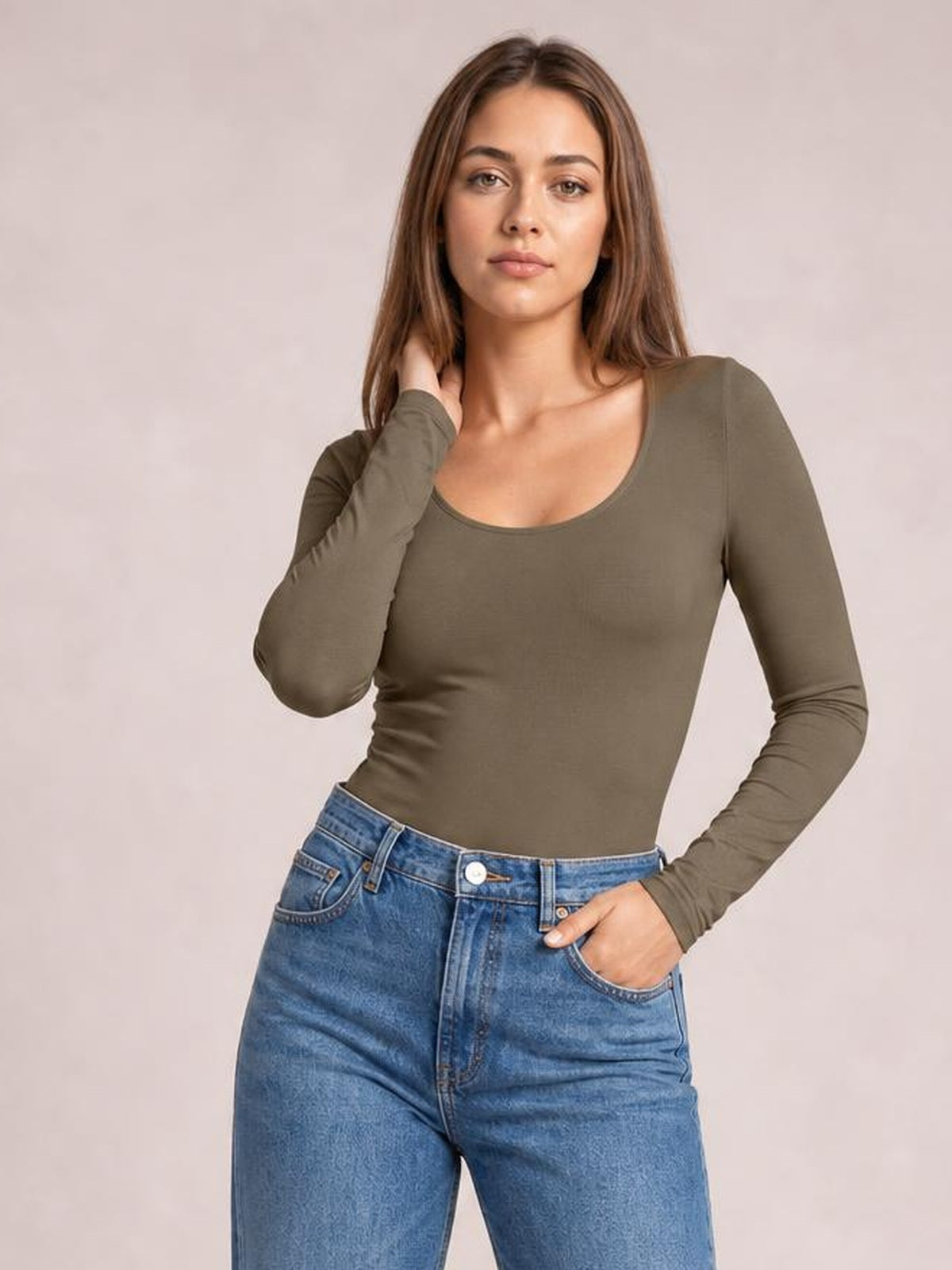 Model poses in a fitted olive round-neck long-sleeve bodysuit with a smooth opaque finish and moderate stretch, paired with blue jeans.