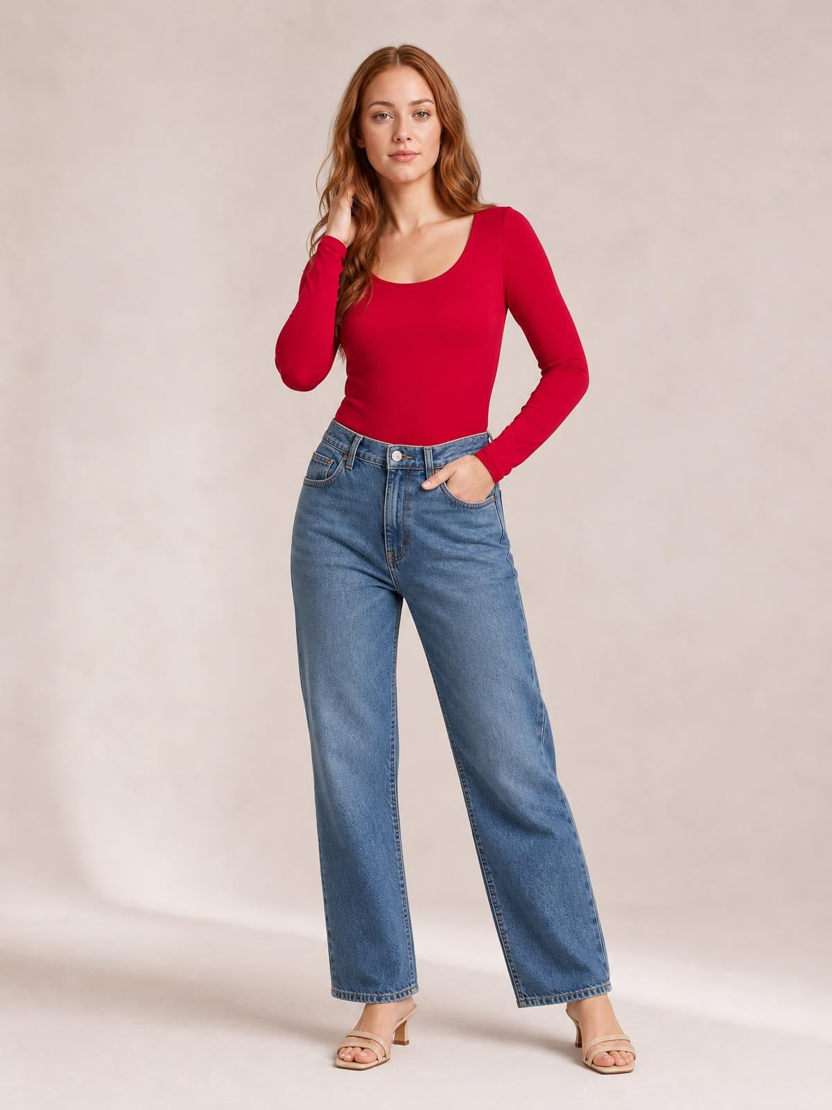 Model poses in a red round neck long sleeve bodysuit with a smooth fitted silhouette, tucked into wide-leg blue jeans.