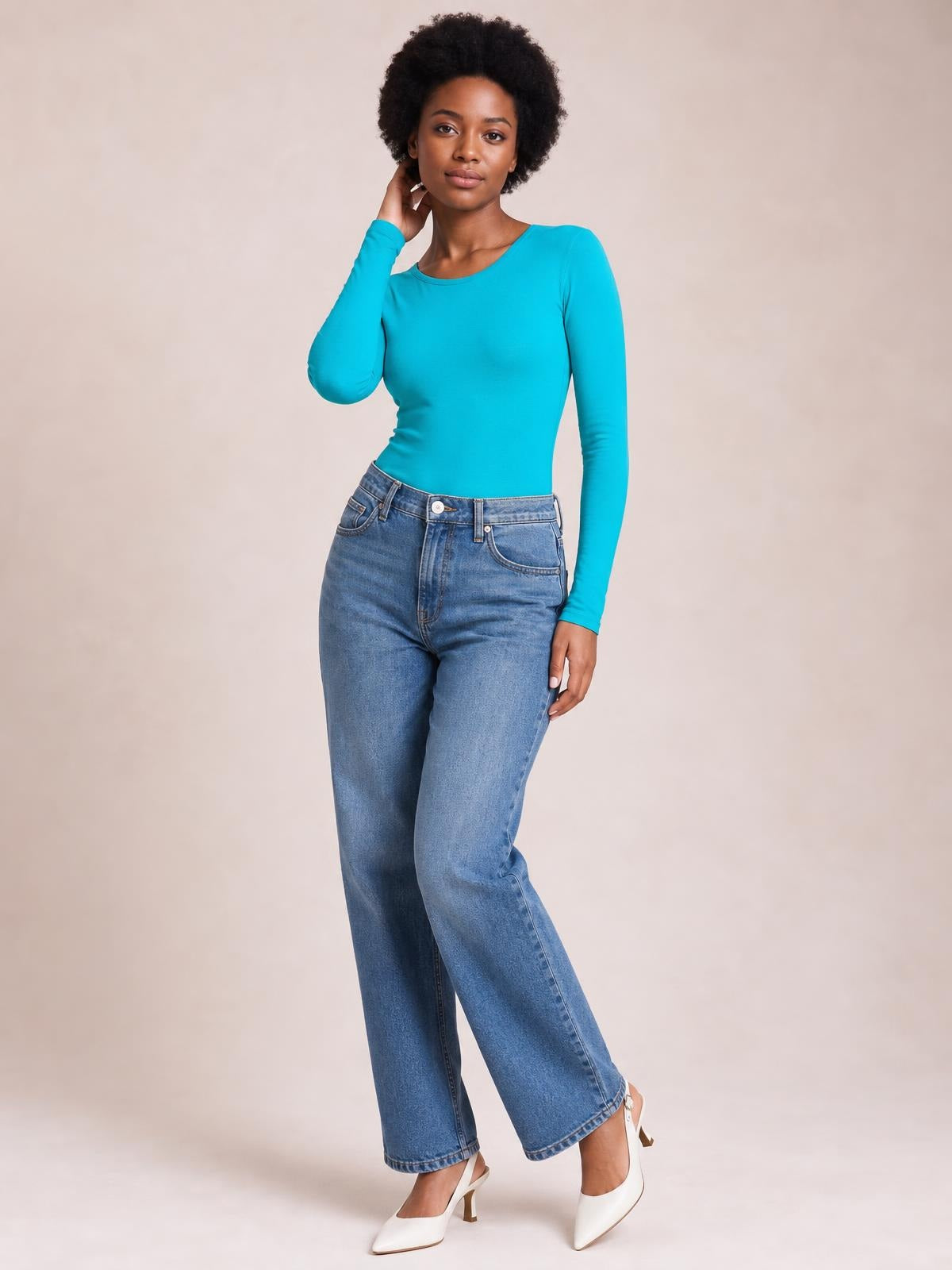 Model wears a turquoise round neck long sleeve bodysuit with a fitted silhouette and smooth opaque construction, posing with one hand at her neck.