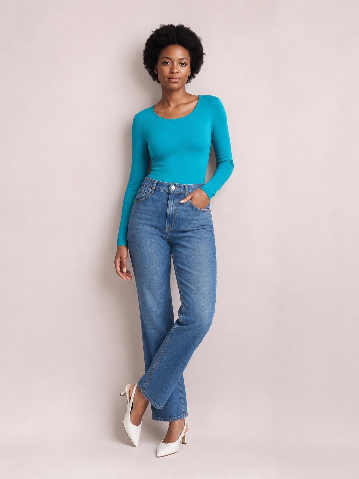Model poses in a turquoise round neck long sleeve bodysuit with a fitted silhouette and smooth construction, paired with wide-leg jeans.