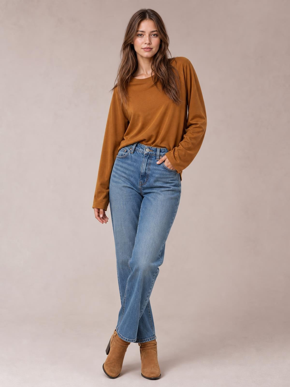 Model wearing a brown round-neck long-sleeve cropped T-shirt with a relaxed silhouette, standing with one hand in her jeans pocket.