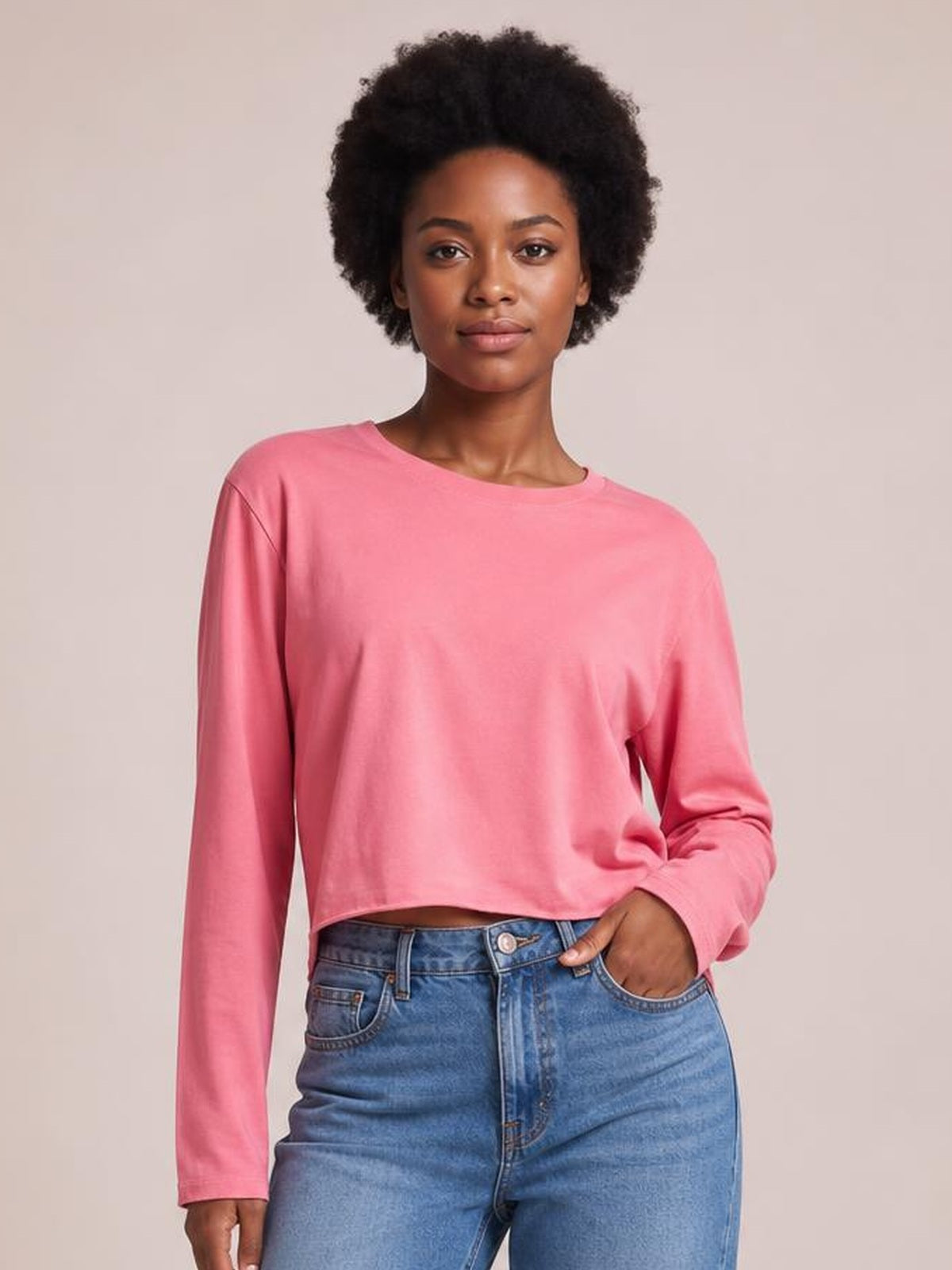 A model poses front-facing in a pink round-neck long-sleeve cropped T-shirt with a relaxed silhouette and straight hem, one hand in her jeans pocket.