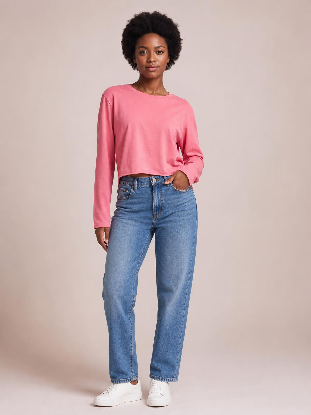 Model wears a pink round neck long sleeve cropped T-shirt with a relaxed straight silhouette and clean hem, posing with one hand in her jeans pocket.