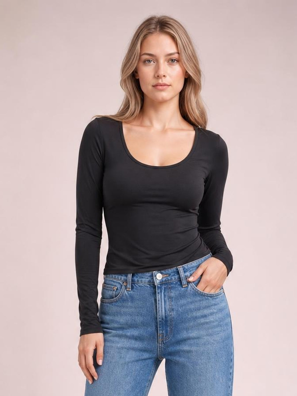 Model wears a black long sleeve T-shirt with a rounded scoop neckline and fitted silhouette, standing front-facing with one hand in her jeans pocket.