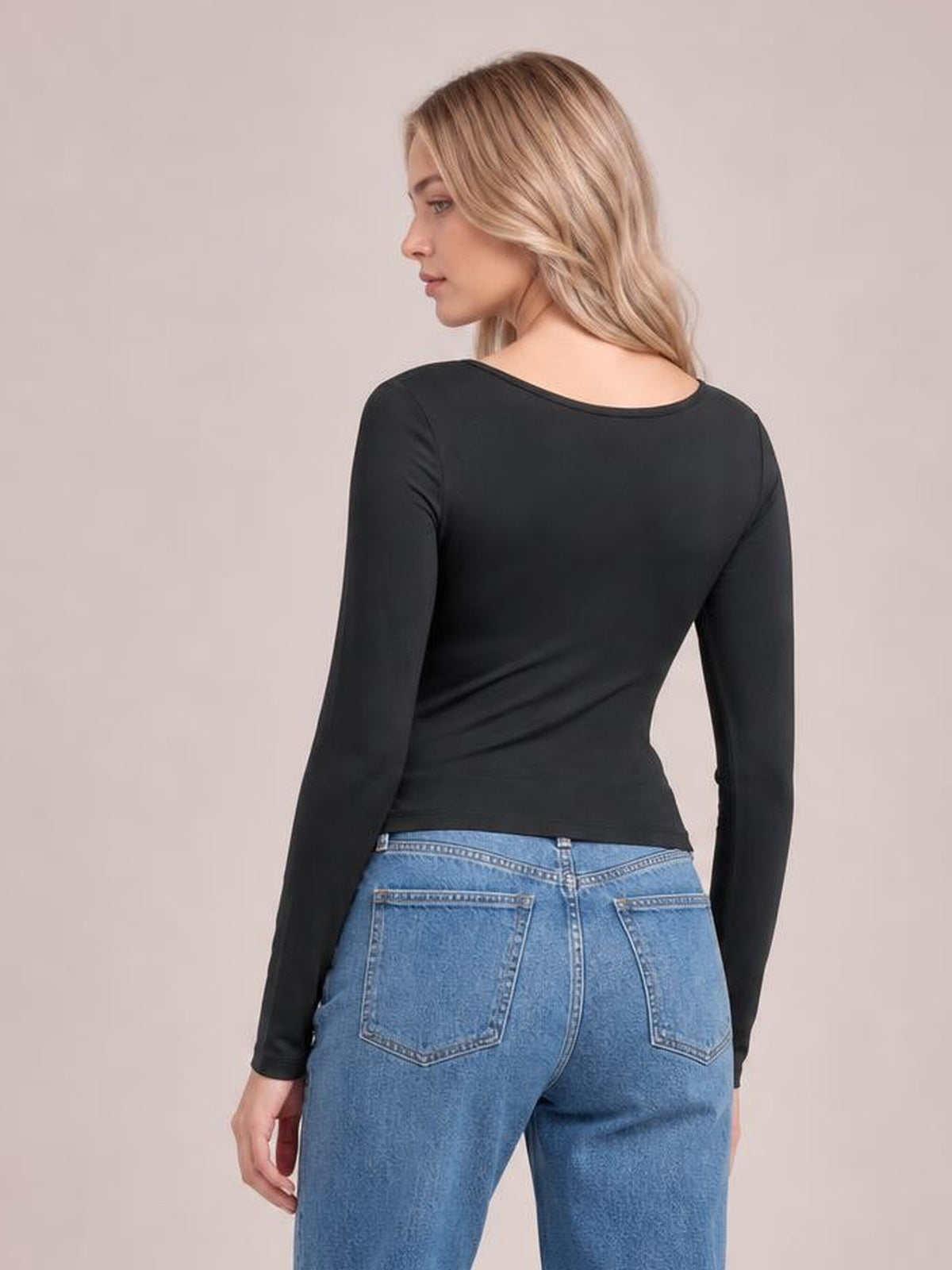 Model turned slightly away to show a black round-neck long-sleeve T-shirt with a fitted silhouette, smooth construction, and straight hem.