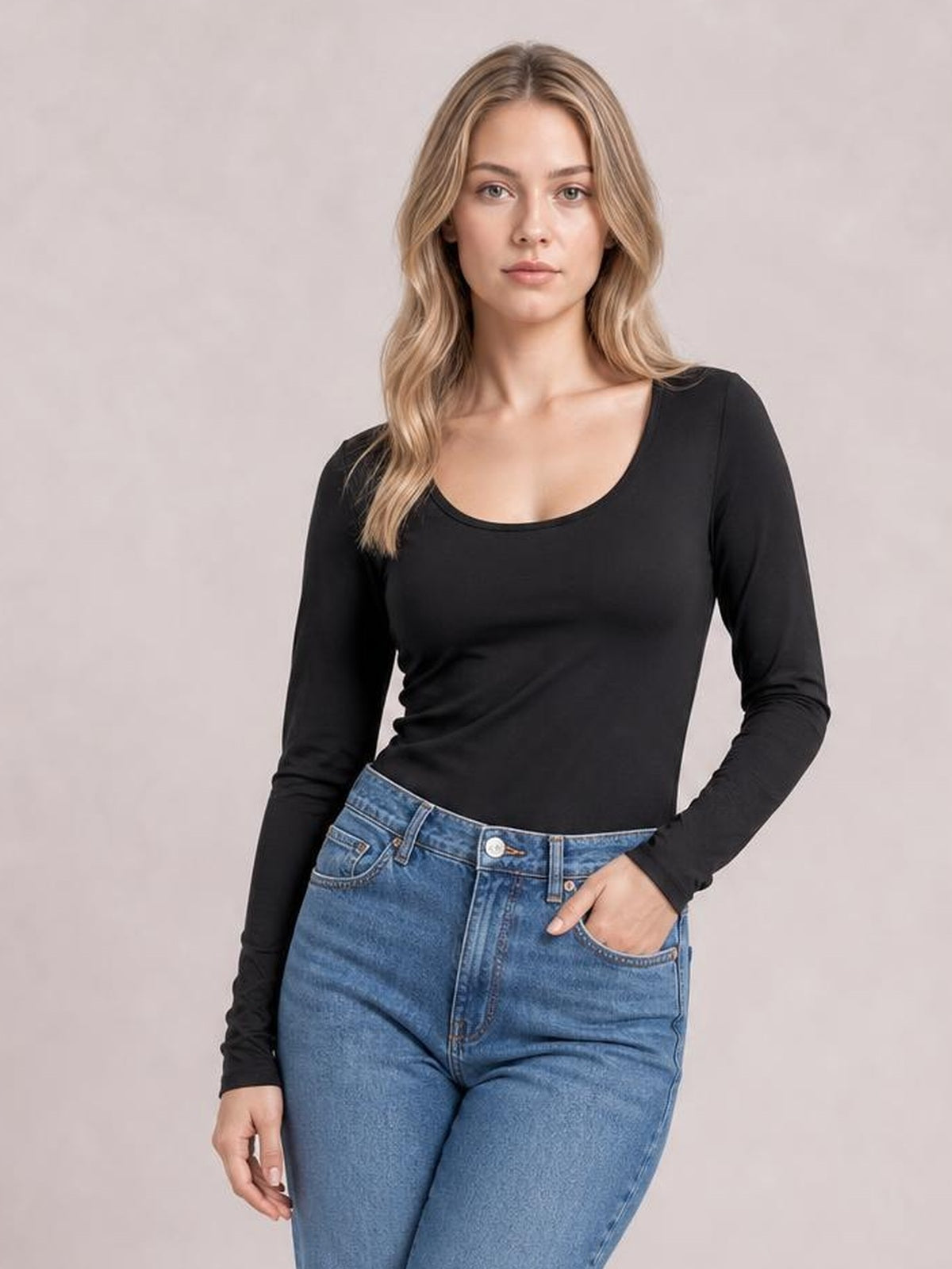 Model wearing a black round neck long sleeve T-shirt with a fitted silhouette and softly scooped neckline, posing with one hand in her jeans pocket.