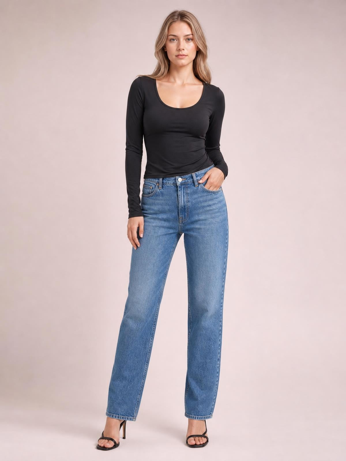 A model wears a black round-neck long-sleeve T-shirt with a fitted silhouette, standing with one hand in her jeans pocket.