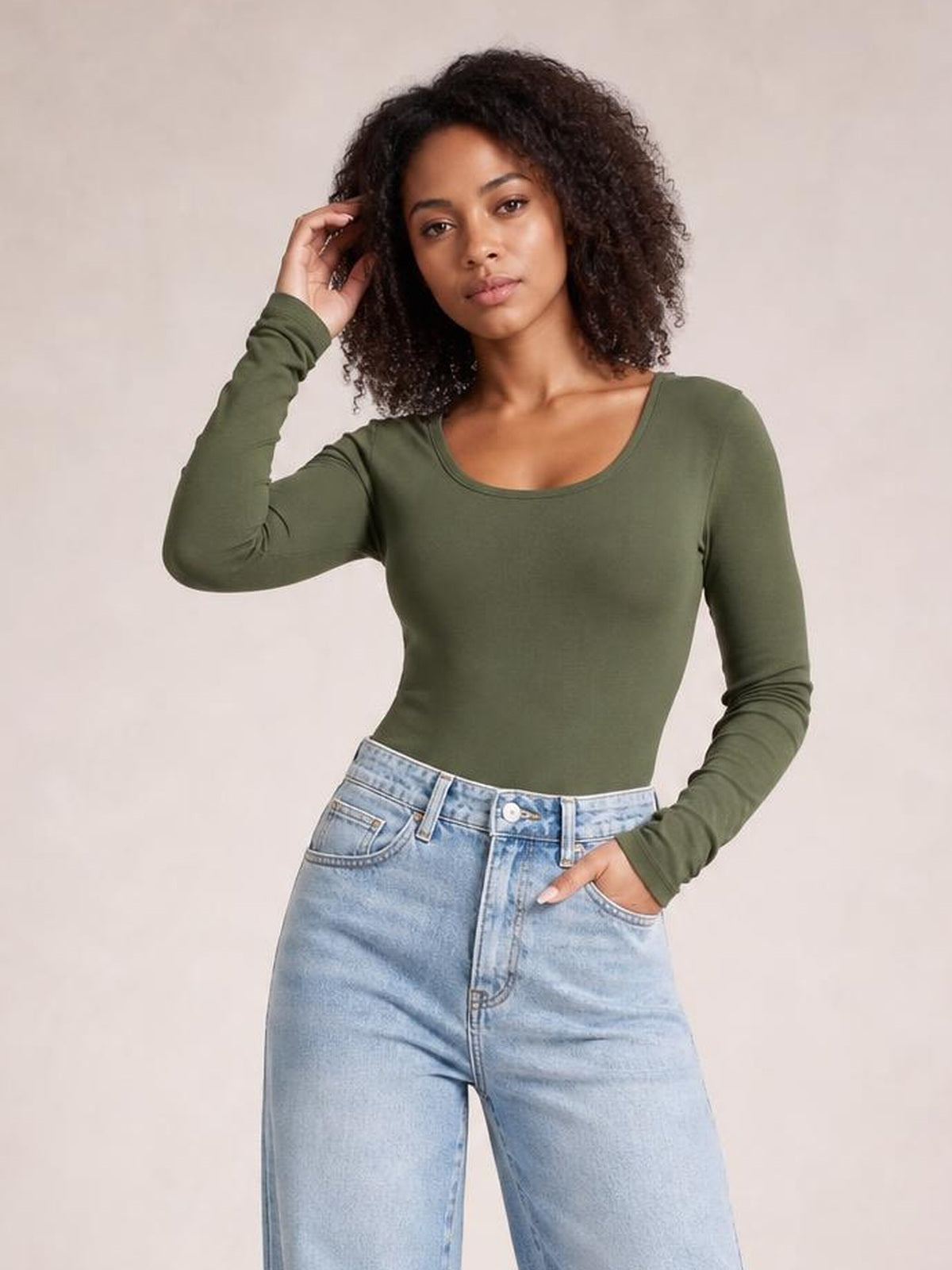 Model poses in an olive green round neck long sleeve T-shirt with a fitted silhouette and slightly stretchy construction, paired with light-wash jeans.