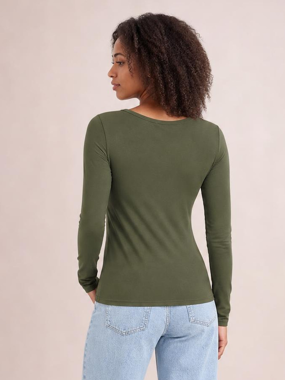A model stands turned away in an olive green round neck long sleeve T-shirt with a smooth, fitted silhouette and slightly stretchy construction.
