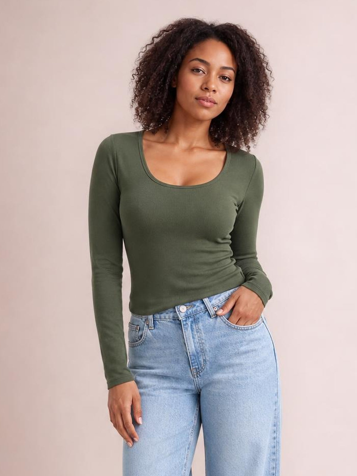 Model wearing an olive green round neck long sleeve T-shirt with a fitted silhouette, standing with one hand in her jeans pocket.