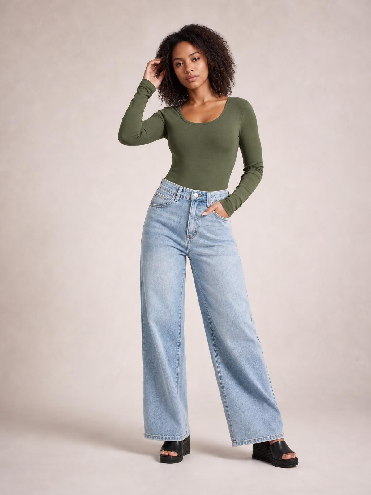 A model poses in an olive-green round-neck long-sleeve T-shirt with a fitted silhouette, one hand in her jeans pocket and the other touching her hair.