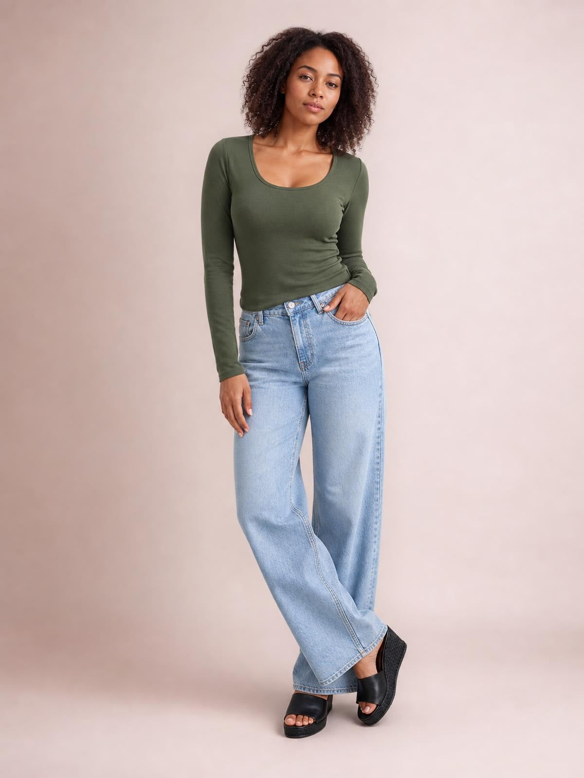 A model poses in an olive green round neck long sleeve T-shirt with a fitted silhouette, slightly stretchy fabric, and one hand tucked into light-wash jeans.
