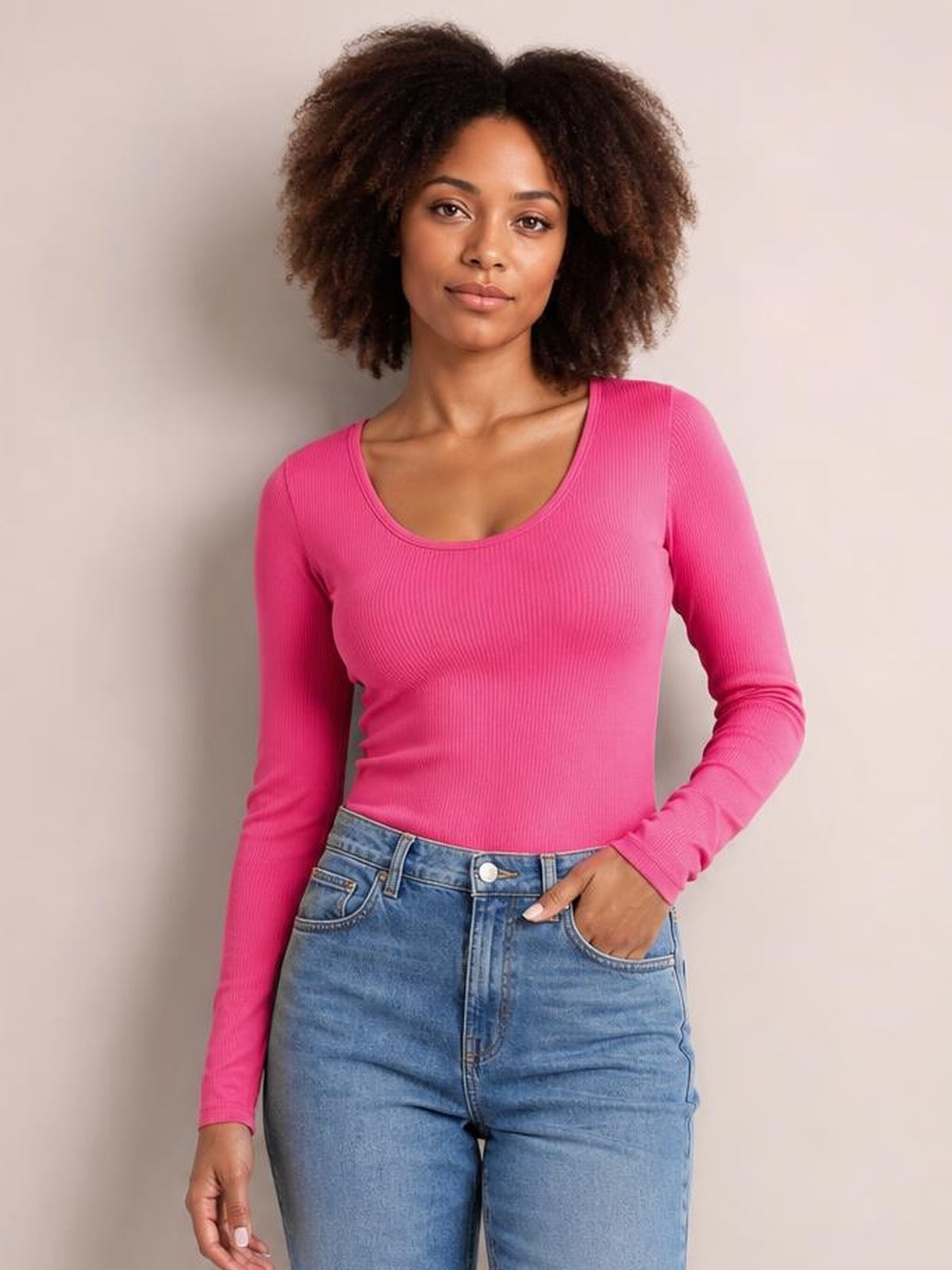 A model poses in a fitted pink round neck long sleeve T-shirt with vertical ribbed texture, gently stretchy silhouette, and one hand resting in her jeans pocket.