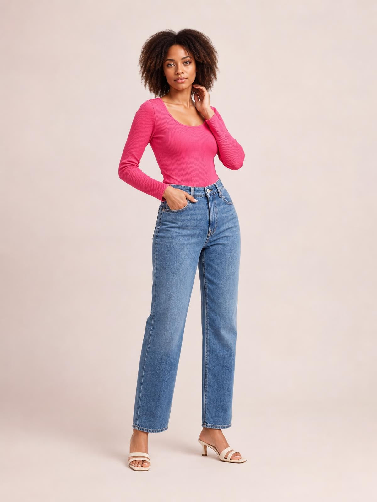 A model poses in a fitted pink round neck long sleeve T-shirt with a ribbed texture and sculpted silhouette, one hand at her waist and the other near her neck.