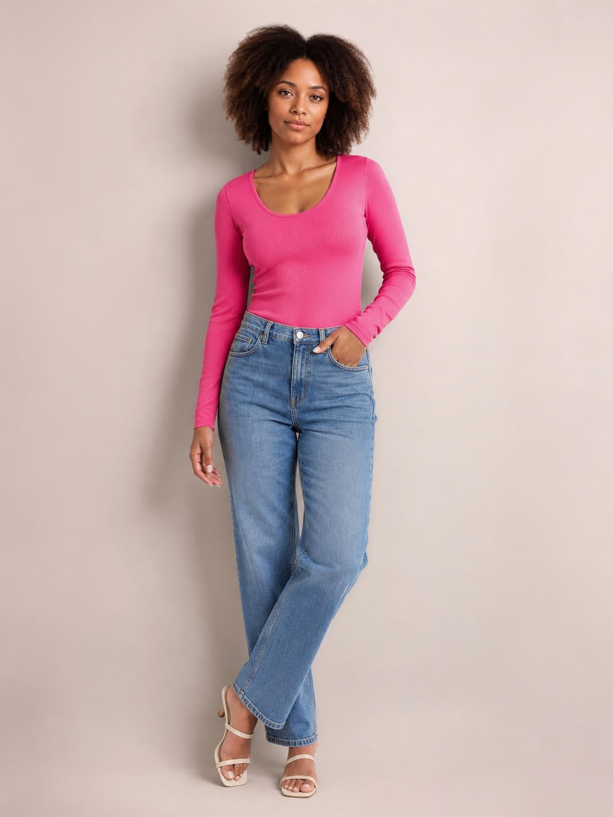 Model poses in a bright pink round neck long sleeve T-shirt with a fitted silhouette and ribbed construction, paired with light-wash jeans.