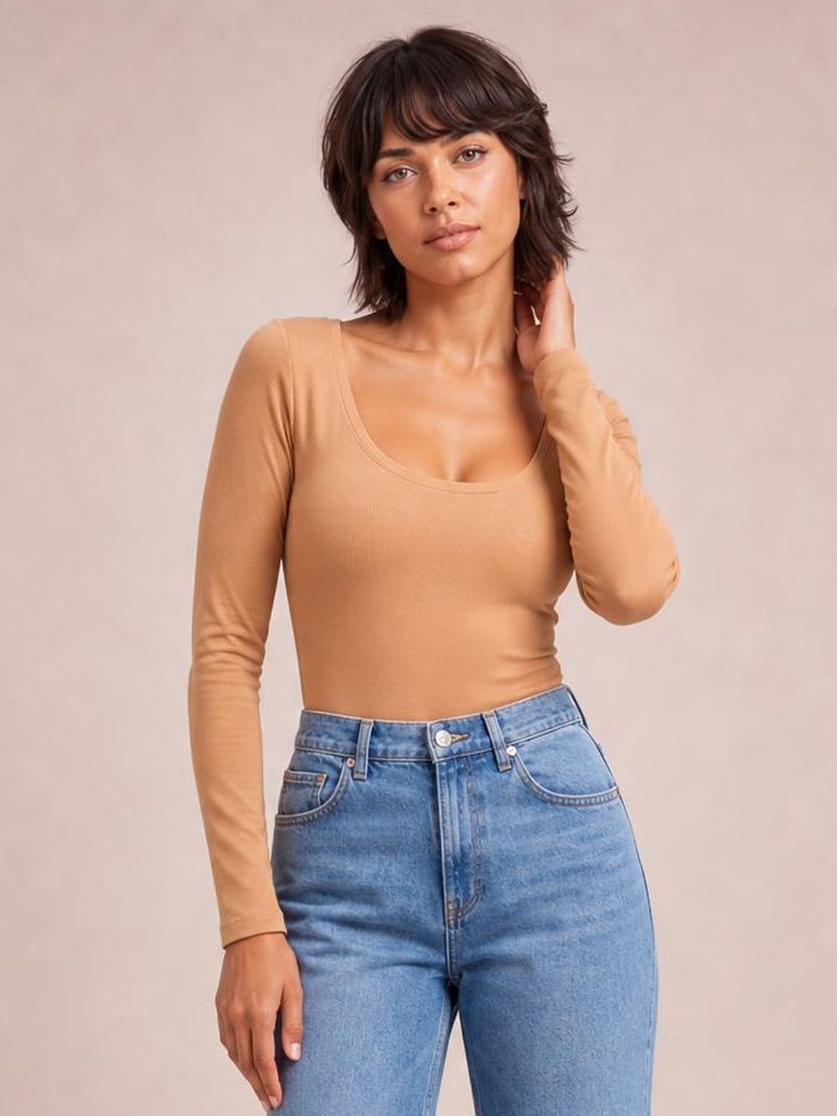 Model poses with one hand near her hair, wearing a fitted tan long-sleeve T-shirt with a wide neckline, smooth construction, and slight stretch.